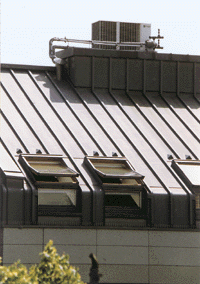 Dynamische Licht/Schatten-Wirkung der Leistendeckung strukturiert die Dachfläche. Links unten ist der Anschluß an die erhöhte Brandwand erkennbar. (Foto: Rheinzink)