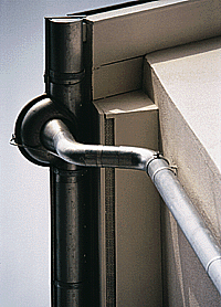 Bild 3: Dachentwässerungsdetail mit halbrunder, vorgehängter Rinne, harmonisch eingepaßter Rinnenerweiterung, trichterförmigem Einlauf und zwei Rohrbogen, die in das kreisförmige Regenfallrohr übergehen. (Foto: Rheinzink)