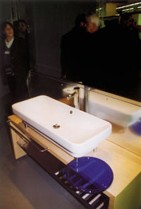 Typisch italienisch: ein ganz flaches, aber geräumiges Waschbecken auf Stahlfüßen über einem Holztisch mit blauer Glasablage und spiegelnden Wandflächen.